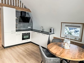 Een moderne keuken met witte kasten, een zwart aanrecht en een ingebouwde oven. Er staat een eettafel met stoelen en een raam met uitzicht op sneeuw.
