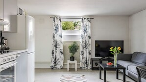 Una cocina moderna con horno empotrado, una zona de comedor con mesa negra y sofá gris, y una sala de estar con televisor de pantalla plana.