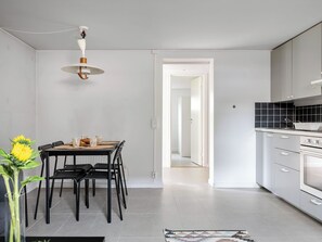 A modern kitchen with a dining area, a hanging light fixture, and a view into another room. - Apartment Odal by Interhome (Halmstad)