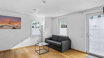 Ein modernes Wohnzimmer mit einem grauen Sofa, einem kleinen Couchtisch und einem Gemälde eines Sonnenuntergangs.