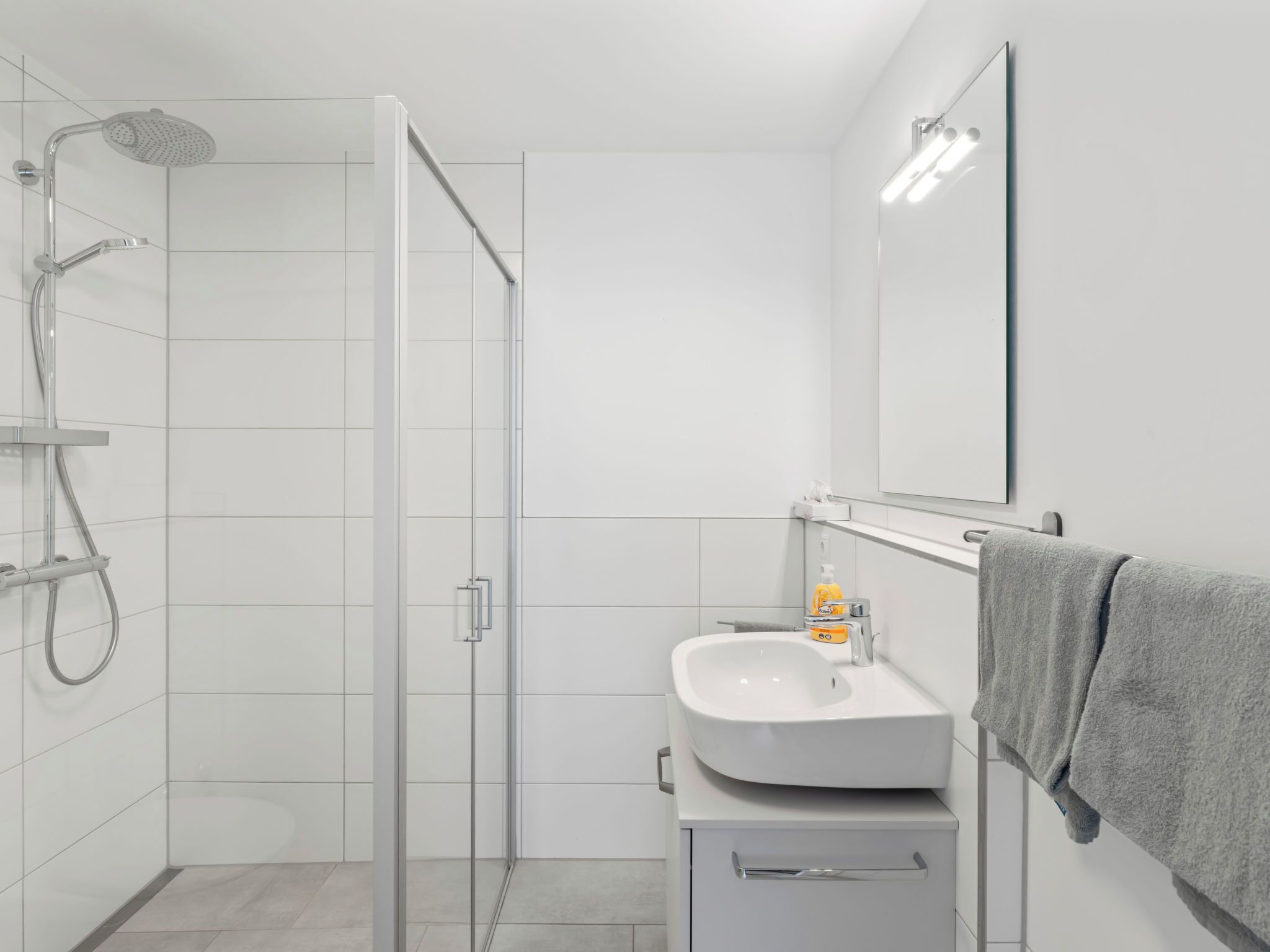 Un baño moderno con cabina de ducha de vidrio, un lavamanos blanco y un espejo.