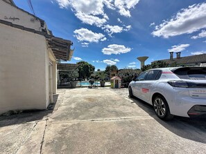 A parking area with a white car, a covered patio with outdoor furniture, a swimming pool, and a building with a sign reading 'La Soufriere.' - La Villa Soleya by Interhome (Rodilhan)