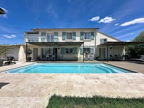 Una casa de dos plantas con piscina, mobiliario de exterior y un patio cubierto.