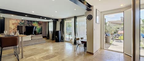 A spacious living area with a sofa, coffee table, and dining table. There is a large window providing a view of the outdoors.