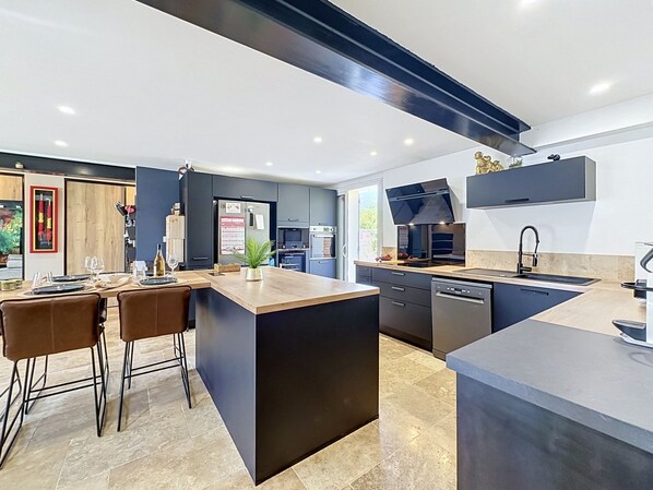 Una cocina moderna con una isla central, muebles oscuros y una zona de comedor con taburetes de bar.