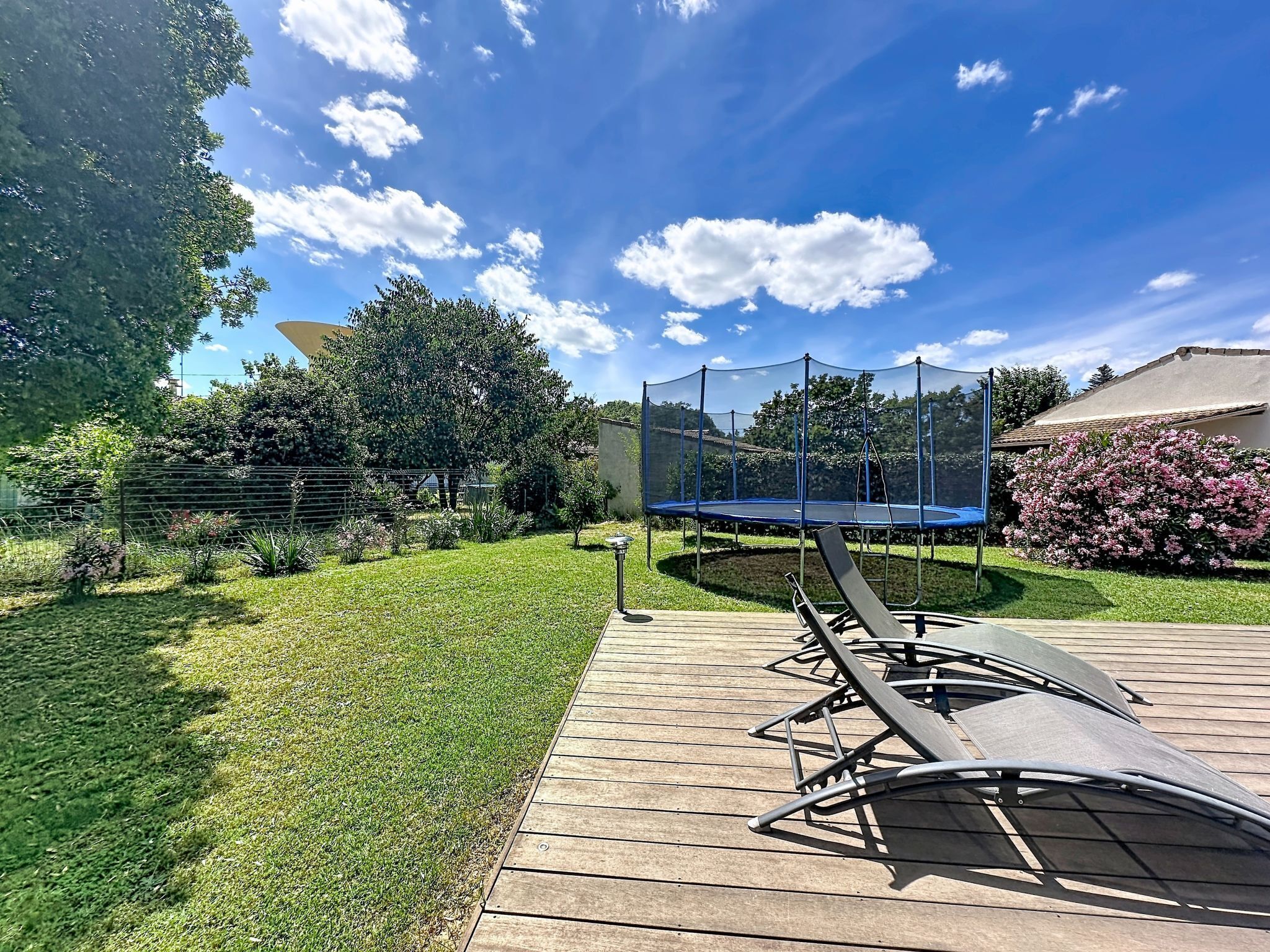 A backyard with a trampoline, a wooden deck, and a garden.