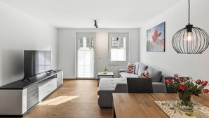 Ein modernes Wohnzimmer mit einer Couch, einem Esstisch, einem Fernseher und einer Küchenzeile.