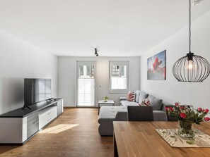 Una sala de estar moderna con un sofá, una mesa de comedor, un televisor y una zona de cocina.