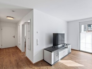 A modern living room with a flat-screen TV on a cabinet, a door leading to another room, and a window with blinds. - Birgit (S2) by Interhome (Endingen am Kaiserstuhl)