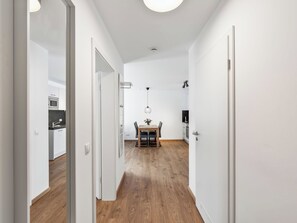 Un estrecho pasillo con suelo de madera, paredes blancas y una zona de comedor con mesa y sillas.