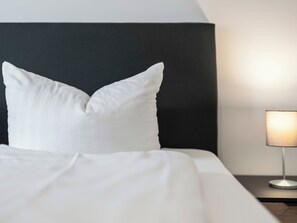 A neatly made bed with white bedding and pillows, a dark headboard, and a bedside lamp on a wooden nightstand. - Christine (S3) by Interhome (Endingen am Kaiserstuhl)