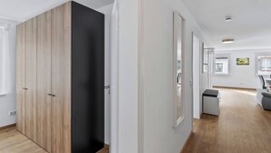 A modern interior with a wooden wardrobe, a white door, and a hallway leading to a room with a window and a chair. - Diana (S4) by Interhome (Endingen am Kaiserstuhl)
