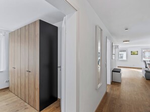 Ein modernes Interieur mit einem Holzschrank, einer weißen Tür und einem Flur, der zu einem Zimmer mit Fenster und Stuhl führt.