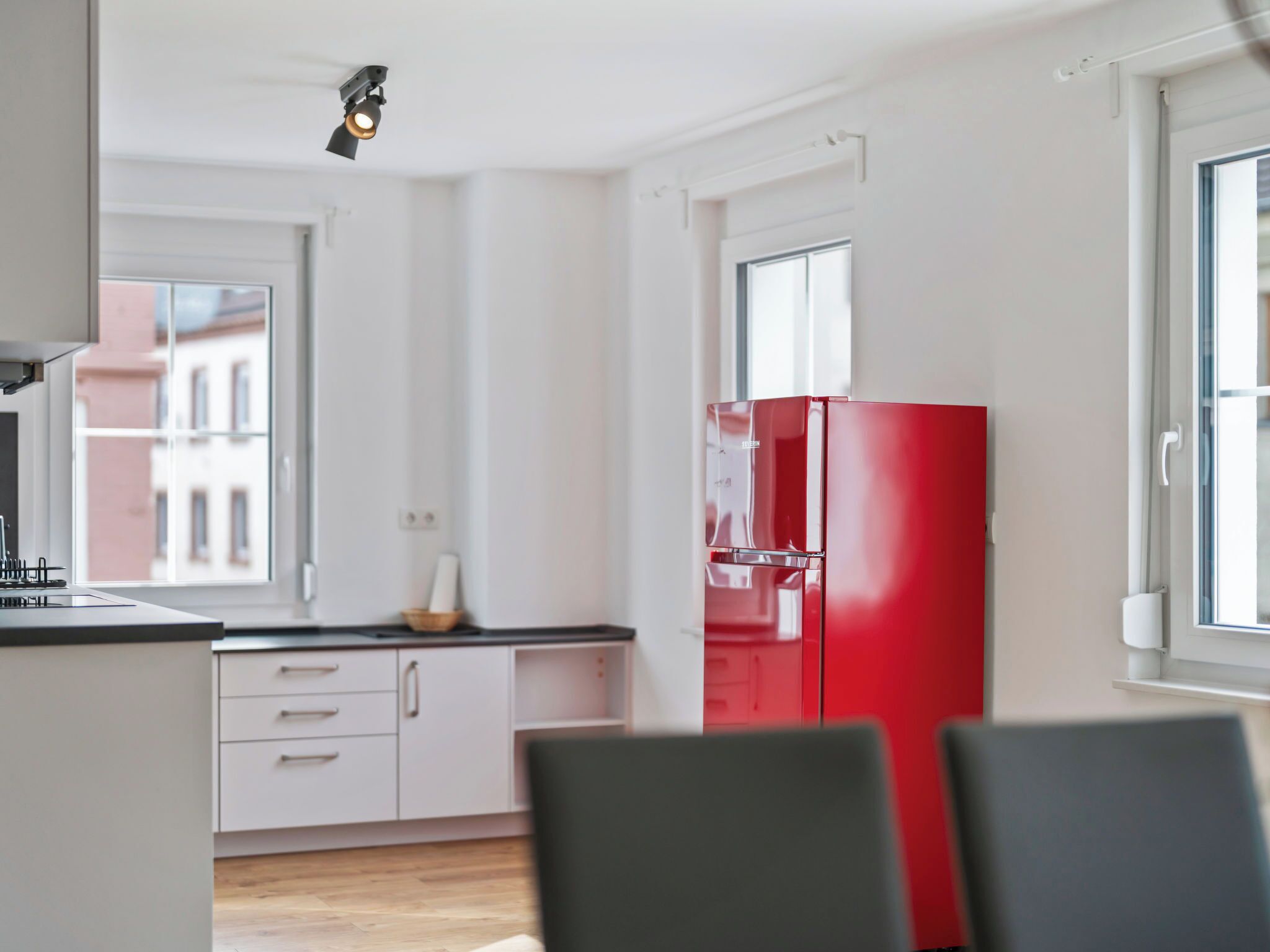 Eine moderne Küche mit weißen Schränken, einem roten Kühlschrank und einem Fenster mit Blick auf Gebäude.
