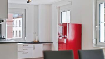Eine moderne Küche mit weißen Schränken, einem roten Kühlschrank und einem Fenster mit Blick auf Gebäude.