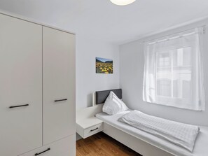 Ein Schlafzimmer mit Bett, Nachttisch, Kleiderschrank, einem Fenster mit Vorhängen und einem Bild an der Wand.