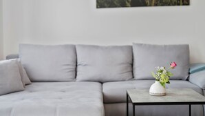 Ein modernes Wohnzimmer mit einem grauen Sofa, einem kleinen Tisch mit Blumen und einem Gemälde von roten Blumen an der Wand.