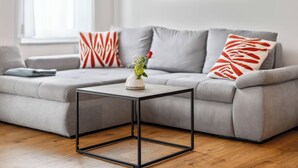 A modern living room with a grey sectional sofa, a small black-framed coffee table, and a vase with flowers. - Fiona (S6) by Interhome (Endingen am Kaiserstuhl)