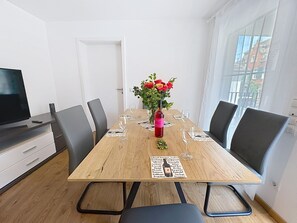 A dining area with a wooden table, black chairs, a vase with flowers, and a bottle of wine.