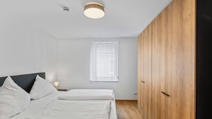 A bedroom with a bed, a nightstand, a window with curtains, and a wooden wardrobe. - Fiona (S6) by Interhome (Endingen am Kaiserstuhl)