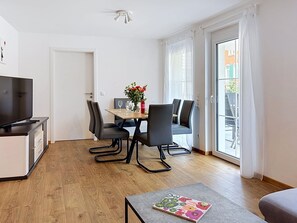 A modern living room with a flat-screen TV, a dining table with chairs, a small sofa, and a balcony with a view. - Fiona (S6) by Interhome (Endingen am Kaiserstuhl)