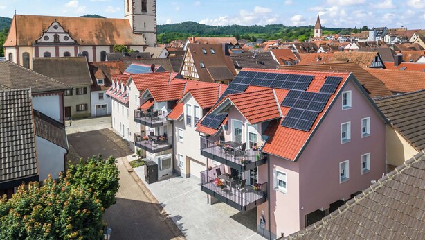Een woonwijk met traditionele architectuur, waaronder een kerktoren, en moderne gebouwen met zonnepanelen.