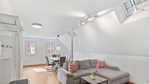 Een moderne woonkamer met een grijze bank, een klein bijzettafeltje en een eethoek op de achtergrond.