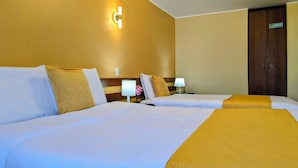 Habitación de hotel con dos camas, una mesita de noche con lámpara, luz en la pared y la puerta de un armario.