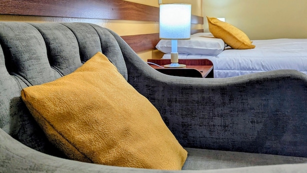 Una habitación de hotel con sofá, mesita de noche con lámpara y cama con almohadas.