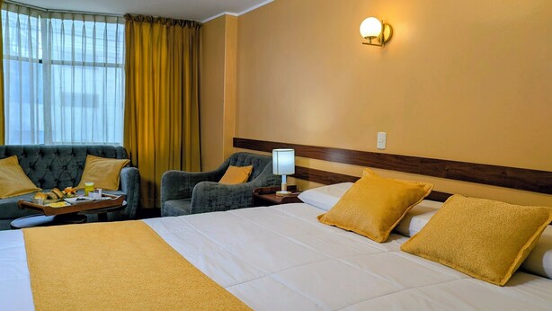 Een hotelkamer met een bed, twee fauteuils, een tafeltje met ontbijtspullen, een nachtkastje met een lamp en een wandlamp.