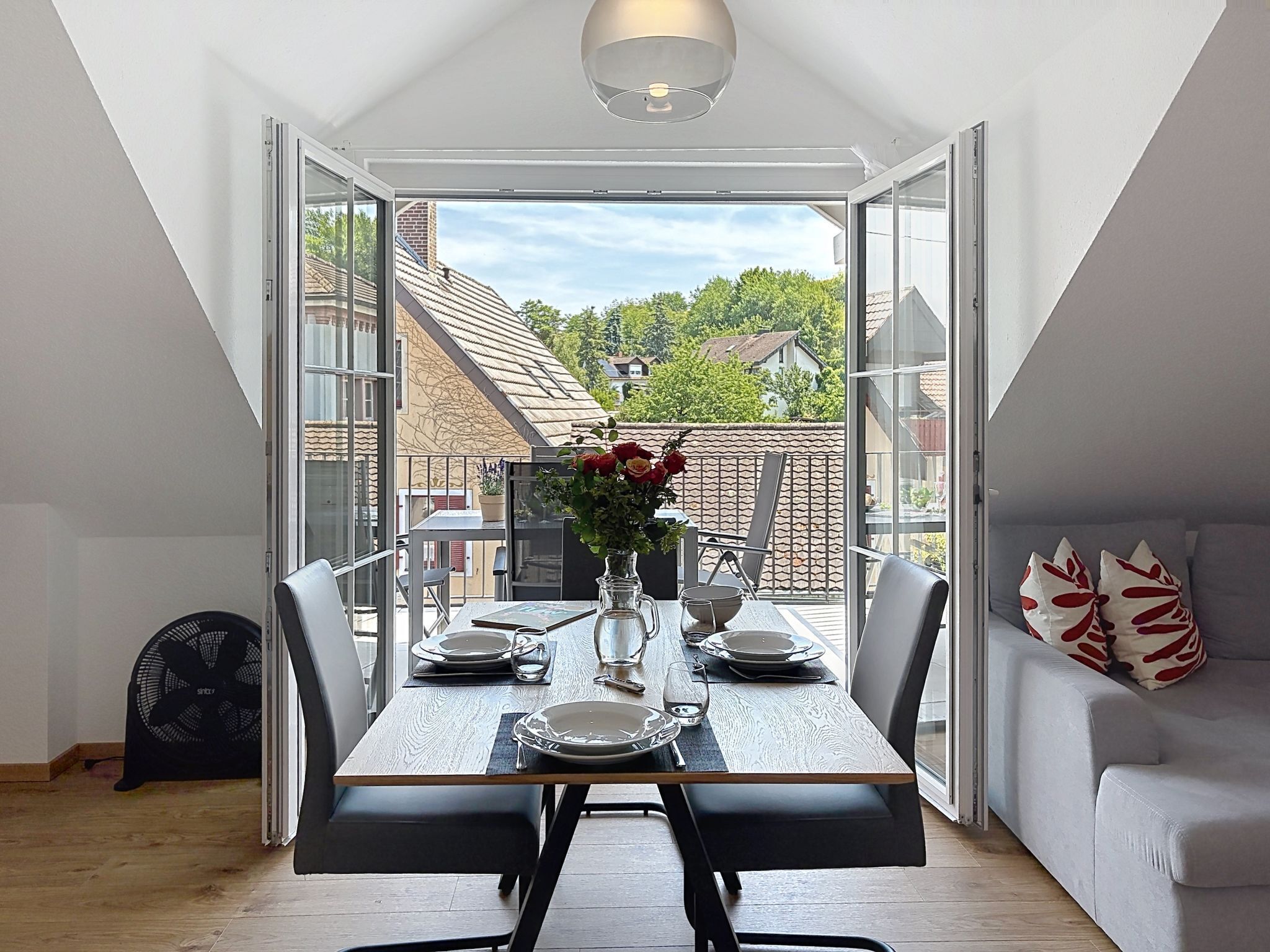 A dining area with a table set for four, a fan, and a sofa with decorative pillows.