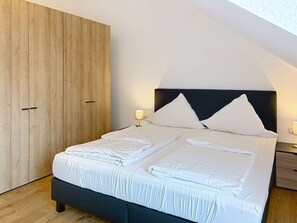 Un lit bien fait, avec des oreillers et des serviettes pliées, une armoire en bois et une table de chevet avec une lampe.