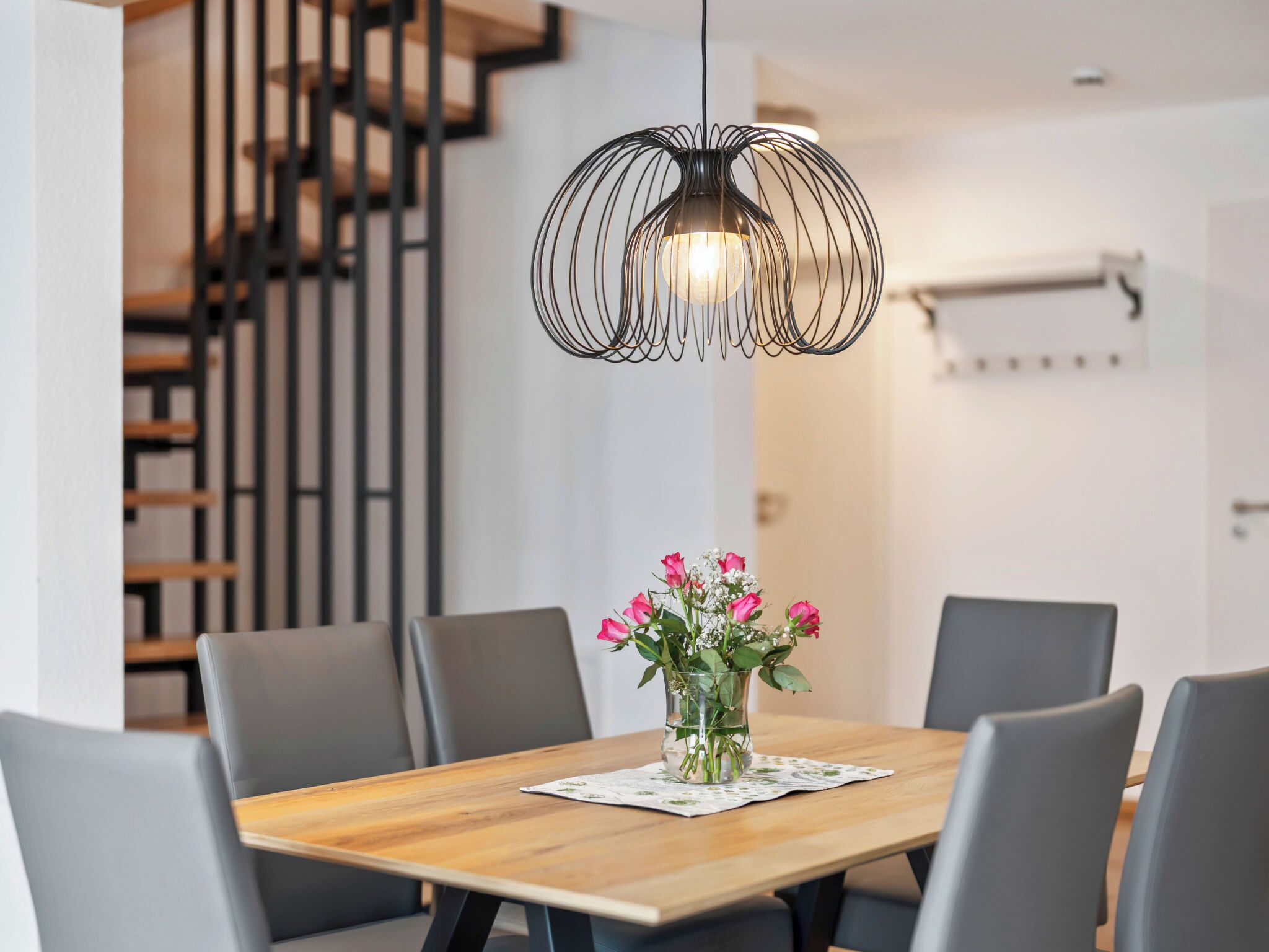 Ein Essbereich mit Holztisch, grauen Stühlen, einer Blumenvase und einer modernen Pendelleuchte.