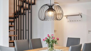 Ein Essbereich mit Holztisch, grauen Stühlen, einer Blumenvase und einer modernen Pendelleuchte.