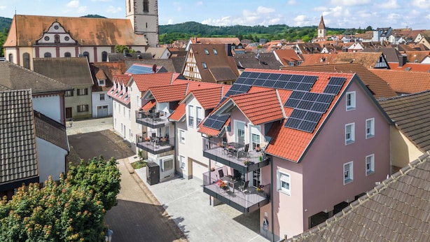 Ein Wohngebiet mit traditioneller Architektur, darunter ein Kirchturm, sowie moderne Gebäude mit Solaranlagen.