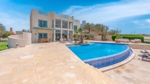 A modern building with a swimming pool, outdoor seating, and palm trees. - Golf Luxury Villa with Private Pool (Red Sea Governorate)