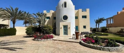 A building with a central dome, a paved courtyard, and palm trees.