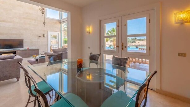A dining area with a glass table, chairs, and a TV in the background. - Golf Luxury Villa with Private Pool (Red Sea Governorate)