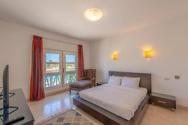 Un dormitorio con cama, una silla, un televisor y un balcón con cortinas.