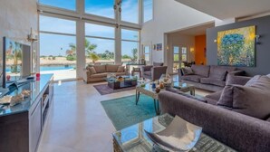A spacious living room with large windows, a sofa set, a coffee table, and a painting on the wall. - Golf Luxury Villa with Private Pool (Red Sea Governorate)
