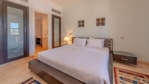 A bedroom with a bed, bedside table, lamp, and a view through a door. - Golf Luxury Villa with Private Pool (Red Sea Governorate)