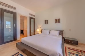 Un dormitorio con cama, mesita de noche, lámpara y vistas a través de una puerta.