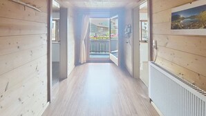 Un pasillo interior de madera con un radiador, una ventana con cortinas y vistas a un balcón con plantas.