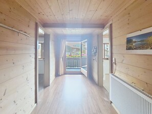 Ein heller Innenraum mit Holzboden, einem Heizkörper, einem Fenster mit Vorhängen und Blick auf einen Balkon mit Pflanzen.