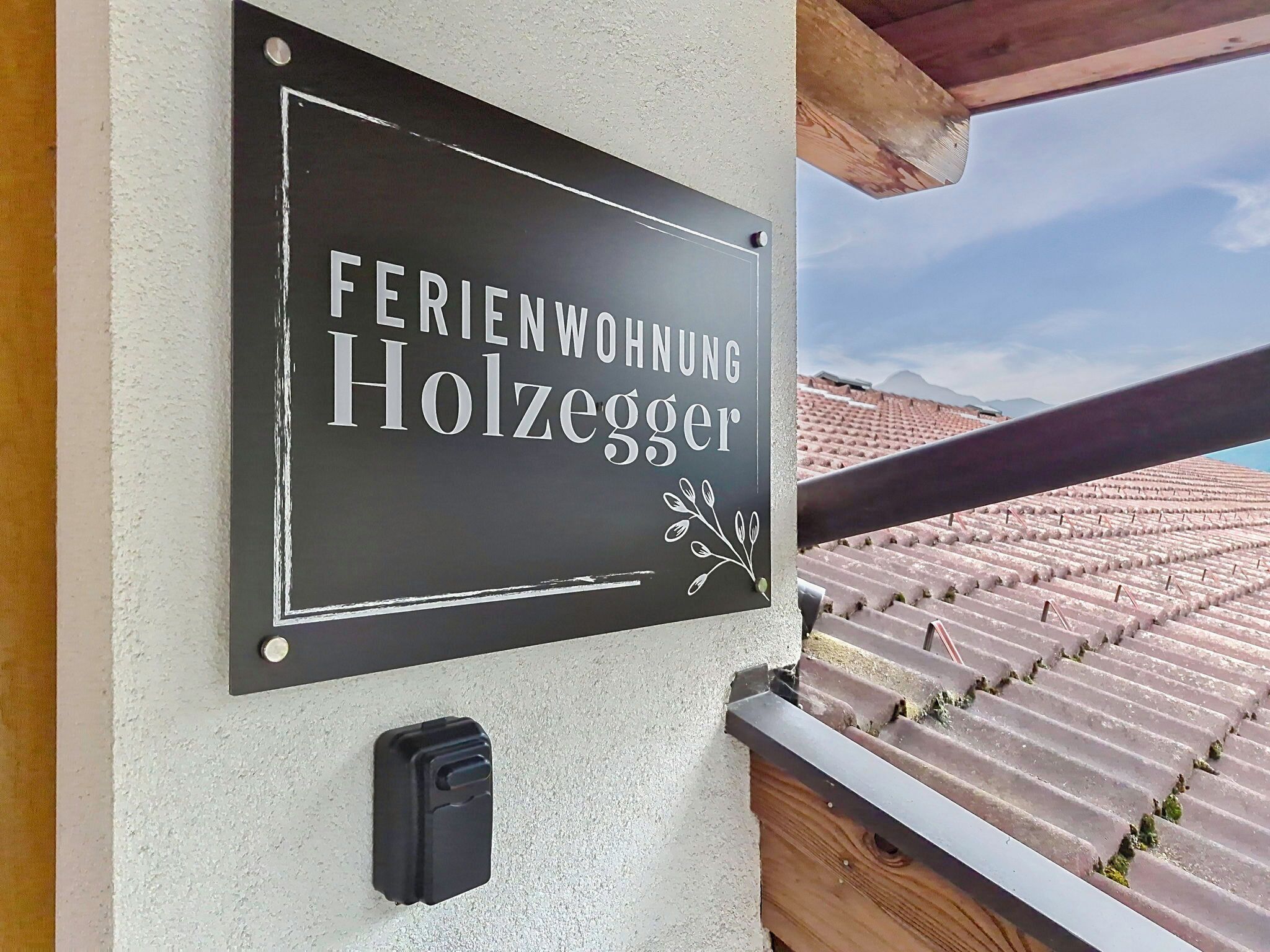 A sign for 'FERIENWOBNUNG Holzegger' with a simple design and a small decorative element.