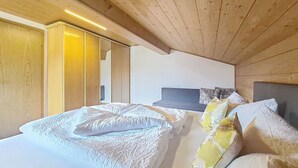 Un dormitorio con techo de madera, cama con ropa blanca y cabecera gris.