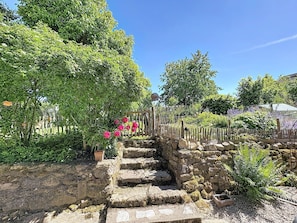 Eine Steintreppe führt zu einem Garten mit üppigem Grün und blühenden Pflanzen.