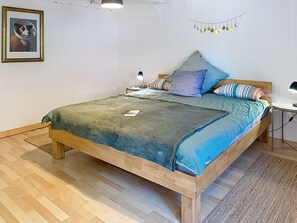 Ein Schlafzimmer mit einem hölzernen Bett, einer grünen Decke, einem gerahmten Bild an der Wand und einer Lichterkette mit Halbmondformen.