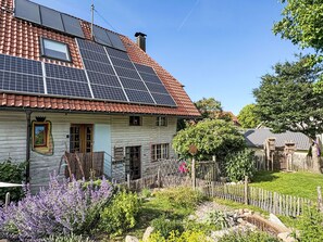 Ein Haus mit Solaranlage auf dem Dach, einem Holzzaun und einem Garten mit verschiedenen Pflanzen.