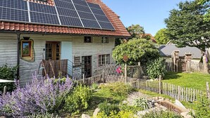 Een huis met zonnepanelen op het dak, een houten hek en een tuin met diverse planten.
